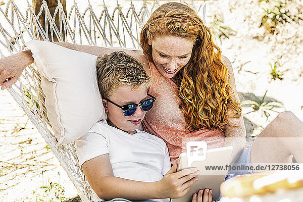 Happy mother and son lying in hammock looking at tablet