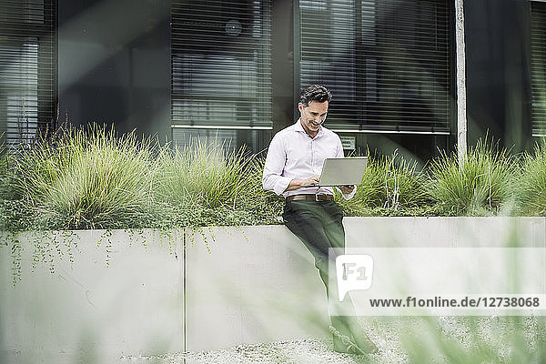 Smiling businessman using laptop outside office building