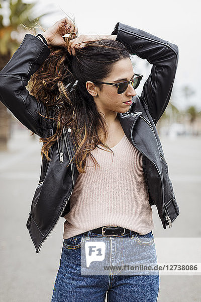 Spain  Barcelona  young woman wearing leather jacket doing her hair
