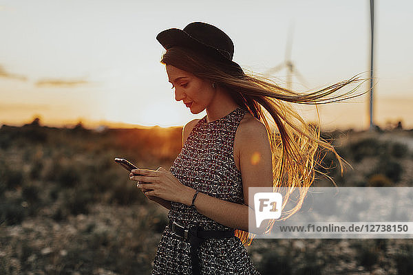 Portrait of young woman looking at cell phone by sunset