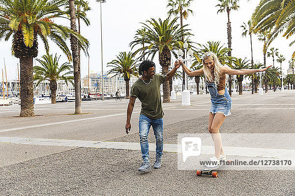 Spain  Barcelona  young man teaching his girlfriend skateboarding