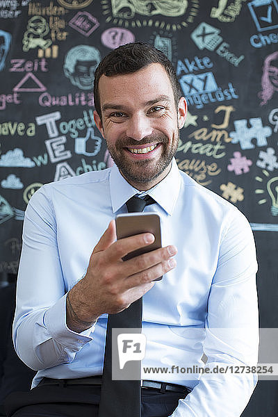 Portrait of smiling businessman with cell phone in creative office