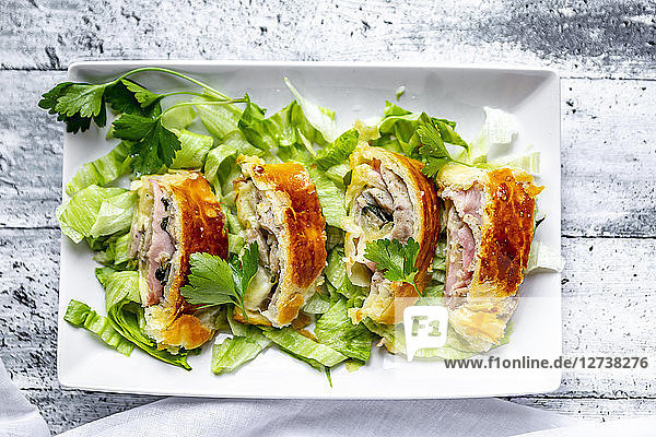 Swiss roll  puff pastry with sausage meat  cheese  onion  parsley and salad on plate