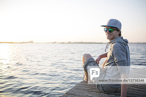 Smiling man sitting on wooden boardwalk at sunset