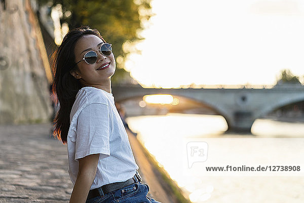France  Paris  portrait of smiling young woman with sunglasses at river Seine at sunset