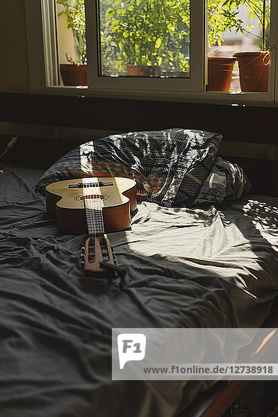 Acoustic guitaron top of a bed with sunlight coming through the window