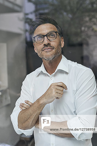 Portrait of man with stubble behind windowpane wearing white shirt and glasses
