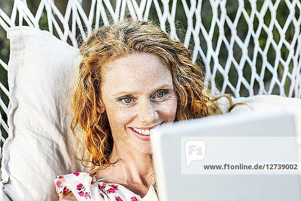 Smiling woman lying in hammock with tablet