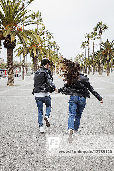 Spain  Barcelona  happy young couple running on promenade with palms