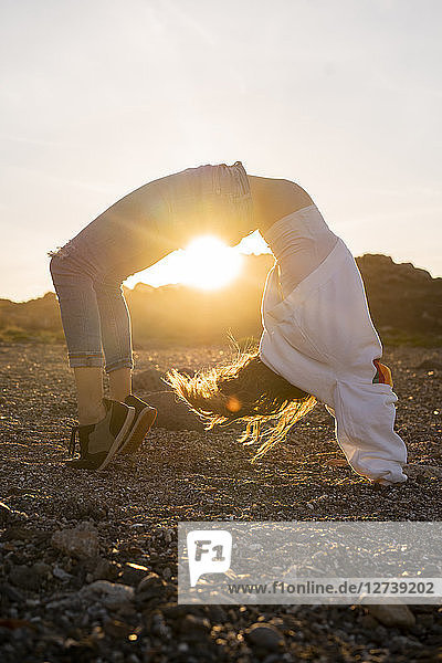 Young woman at the beach  doing wheel pose at sunset