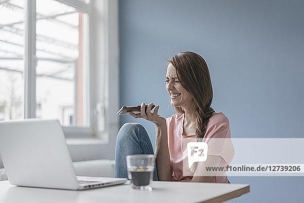 Woman at home sitting at desk with laptop  using smartphone