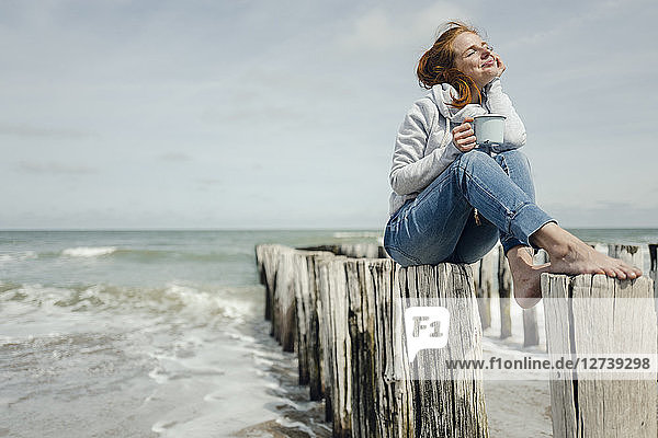 Woman sitting on fence at the sea  drinking tea