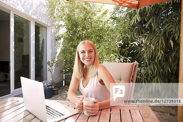 Young smiling woman using laptop  sitting on garden table