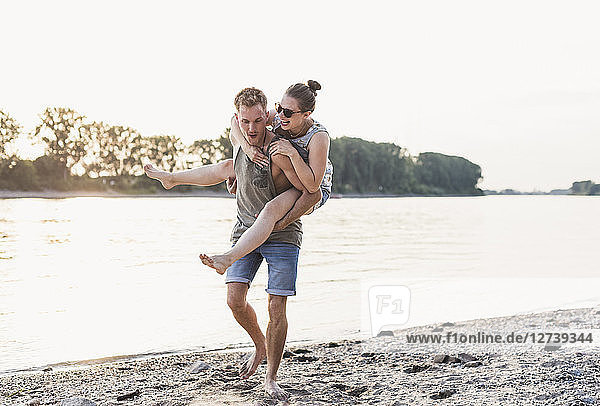 Young man giving girlfriend piggyback ride at the riverbank