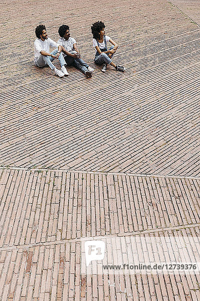 Three friends sitting on a square watching something