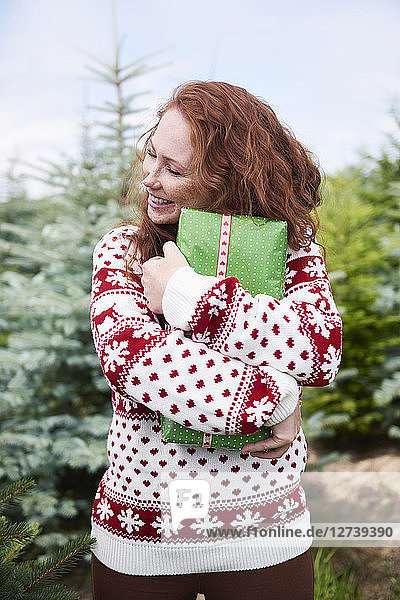Happy redheaded young woman embracing Christmas present outdoors