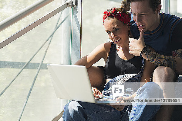 Young couple sitting on stairs using laptop