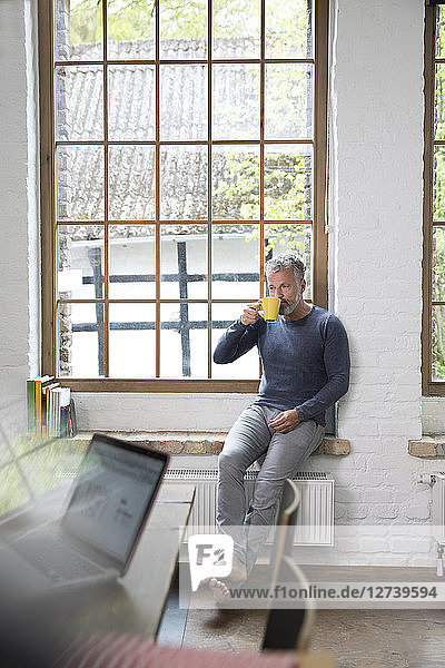 Mture man taking a break  drinking coffee at the window of his loft apartment