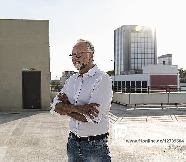 Mature man standing on roof of a high-rise building with arms crossed