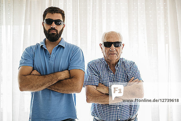 Portrait of adult grandson and his grandfather wearing sunglasses at home