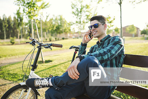 Young man telephoning with his smartphone on park bench