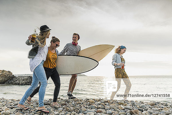 Happy friends with surfboards walking on stony beach