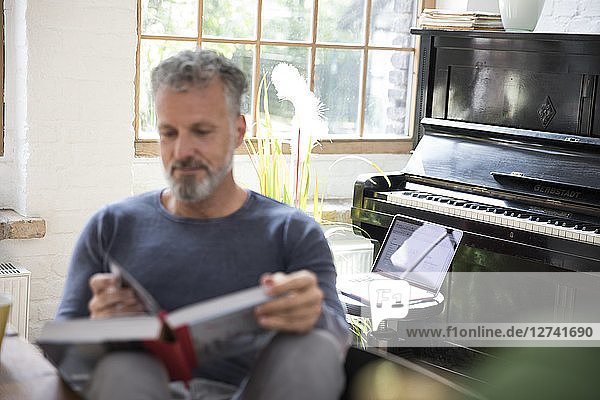 Laptop on stool in front of piano  man reading in book