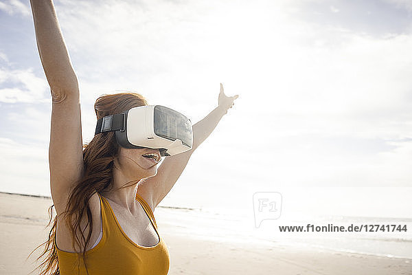 Redheaded woman using VR glasses on the beach