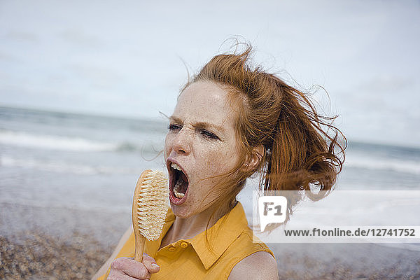 Woman using hair brush at the sea as a microphone