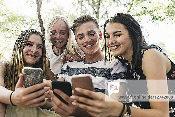 Group of smiling friends looking at cell phones outdoors