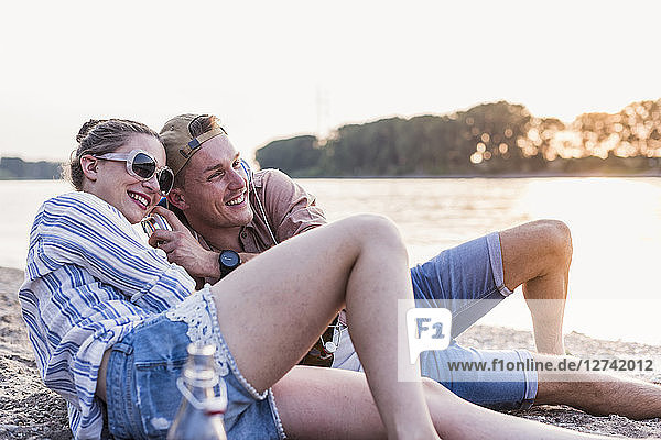 Young couple relaxing at the riverbank sharing headphones
