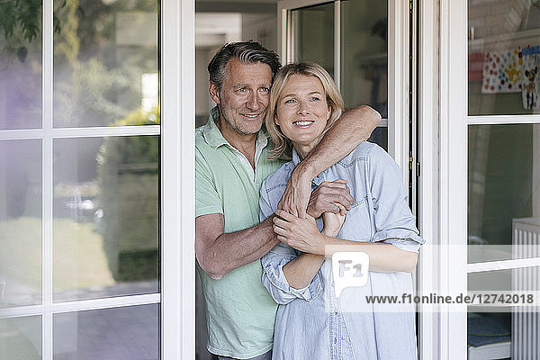 Happy mature couple hugging at French window