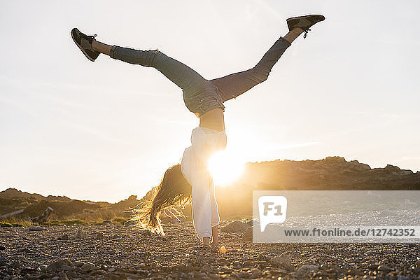 Young woman at the beach  doing handstand at sunset
