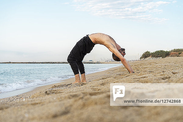 Spain. Man doing yoga on the beach in the evening  upward bow