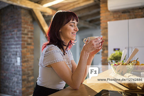 Smiling woman drinking cup of coffee in kitchen at home