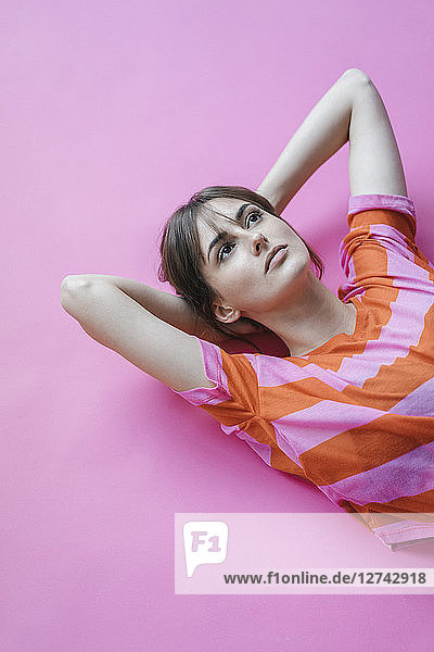 Woman lying on pink background with hands behind head  thinking