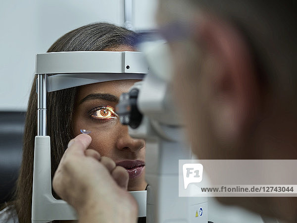 Optometrist examining young woman's eye  contact lens on index finger