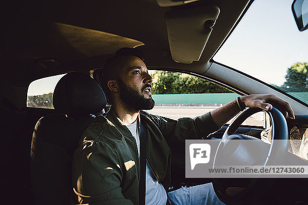 Bearded young man looking at rear-view mirror while driving car