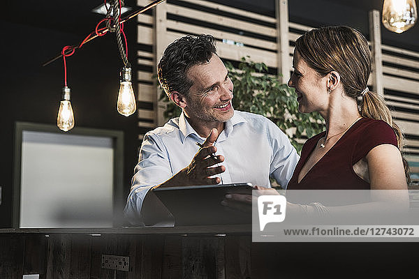 Smiling businesswoman and businessman with tablet discussing in office