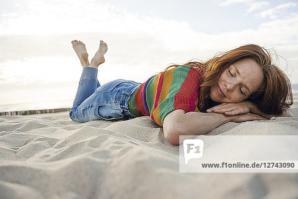 Redheaded woman lying in sand on the beach  with eyes closed