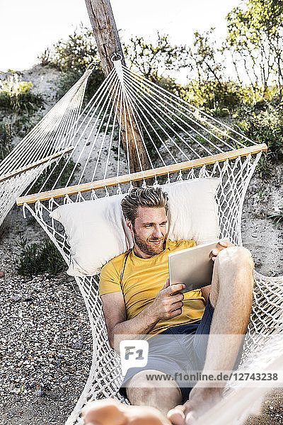 Man lying in hammock using tablet