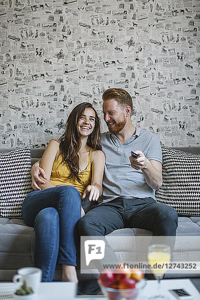 Laughing couple sitting on couch watching TV