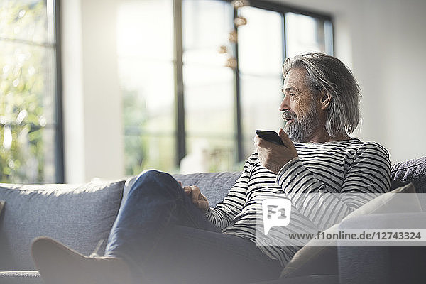 Senior man sitting on couch  using smartphone