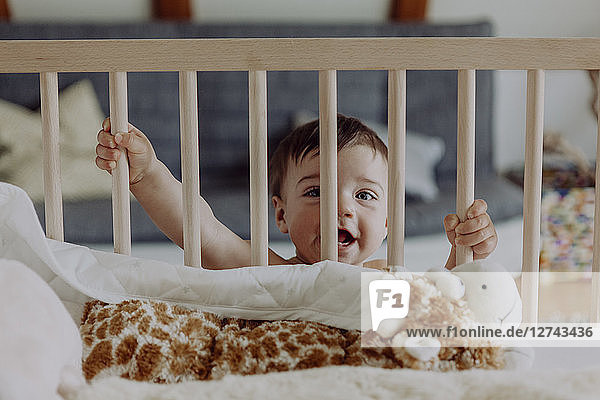 Baby boy holding on to his cot laughing