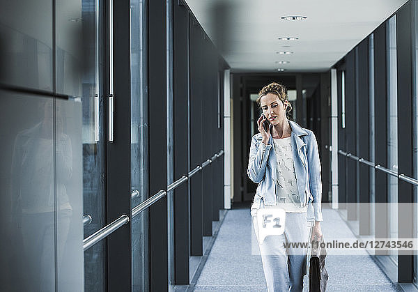 Businesswoman on cell phone walking in office passageway