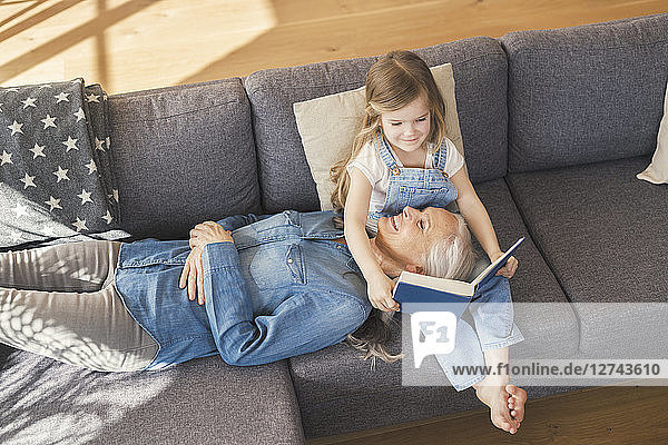 Grandmother and granddaughter sitting on couch  reading together a book