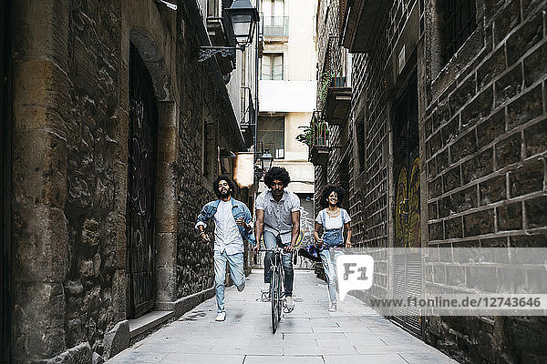 Spain  Barcelona  man riding bicycle down an alley while his friends running behind him