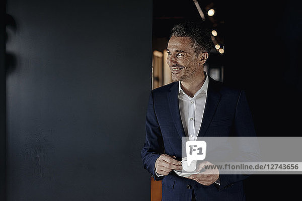 Smiling businessman with espresso cup looking sideways