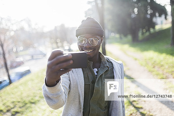 Young man standing in park  taking smartphone selfie