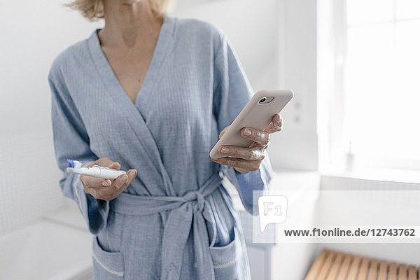 Close-up of woman with cell phone and toothbrush in bathroom